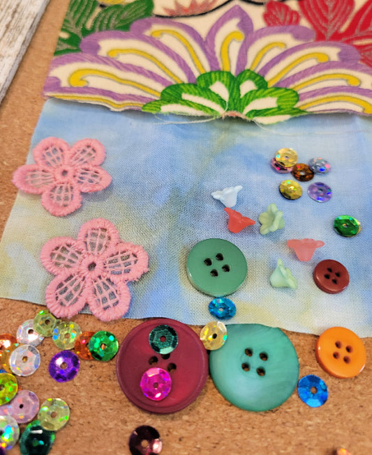 Colorful buttons and flowers on a textured surface with a hand dyed fabric background.