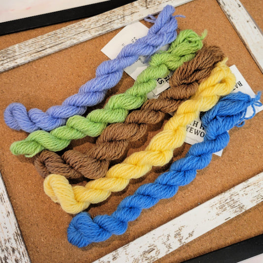 Five twisted tapestry yarn skeins in pastel and bright colors arranged on a cork board: lavender, light green, medium brown, pale yellow, and royal blue.