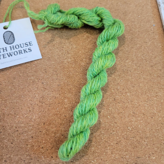 Green tapestry yarn skein on a brown surface with a Bath House Dyeworks label in the background