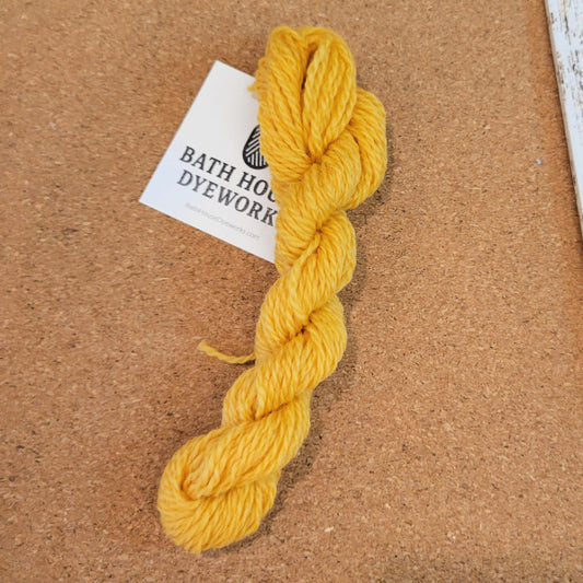 Goldenrod Yellow skein of tapestry yarn with a Bath House Dyeworks label on a brown background