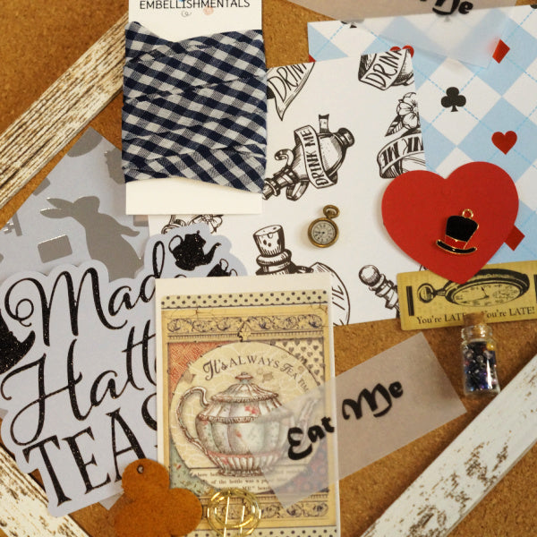 Flat lay of Alice in Wonderland Mini Kit contents including printed cardstock, heart tags, charms, and plaid seam binding.