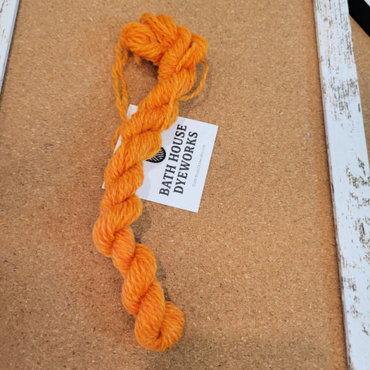 Orange tapestry yarn skein on a cork board with a label for Bath House Dyeworks.